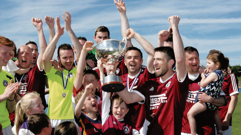 Athenry FC captain Jamie O'Driscoll celebrates with his team-mates Ryan Shaughnessy, Alan O'Donovan, Antoine Ó Conghaile, Gary O'Donnell, Darragh Murphy, Cathal Fahy and Gary Delaney, and young fans, having been presented with the Connacht Junior Cup following their victory over Ballinasloe Town in Lecarrow on Sunday. Photo: Eirefoto.