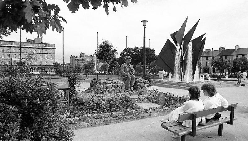 Resting in his original perch in 1985, Sean Phádraic was a focal point of the old Eyre Square. He was removed during the revamp of the Square in 2004. A bronze replica Ó Conaire statue is currently in Eyre Square, but has not yet been unveiled. Also in the photograph is the commemorative fountain in the shape of Galway Hooker sails erected in 1984 to mark Galway's quincentenary.