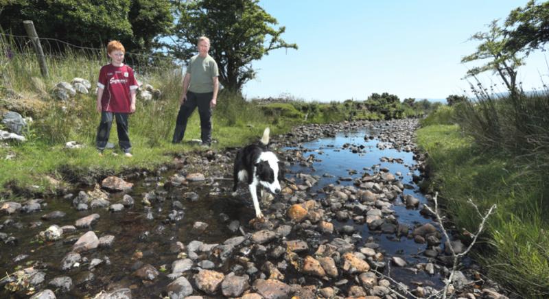 Sheepdog Bella crosses the Bunnaun Stream, without getting his paws wet, as John Geoghegan and son Seán, look at the water levels dropping by the day. PHOTO: JOE O’SHAUGHNESSY.